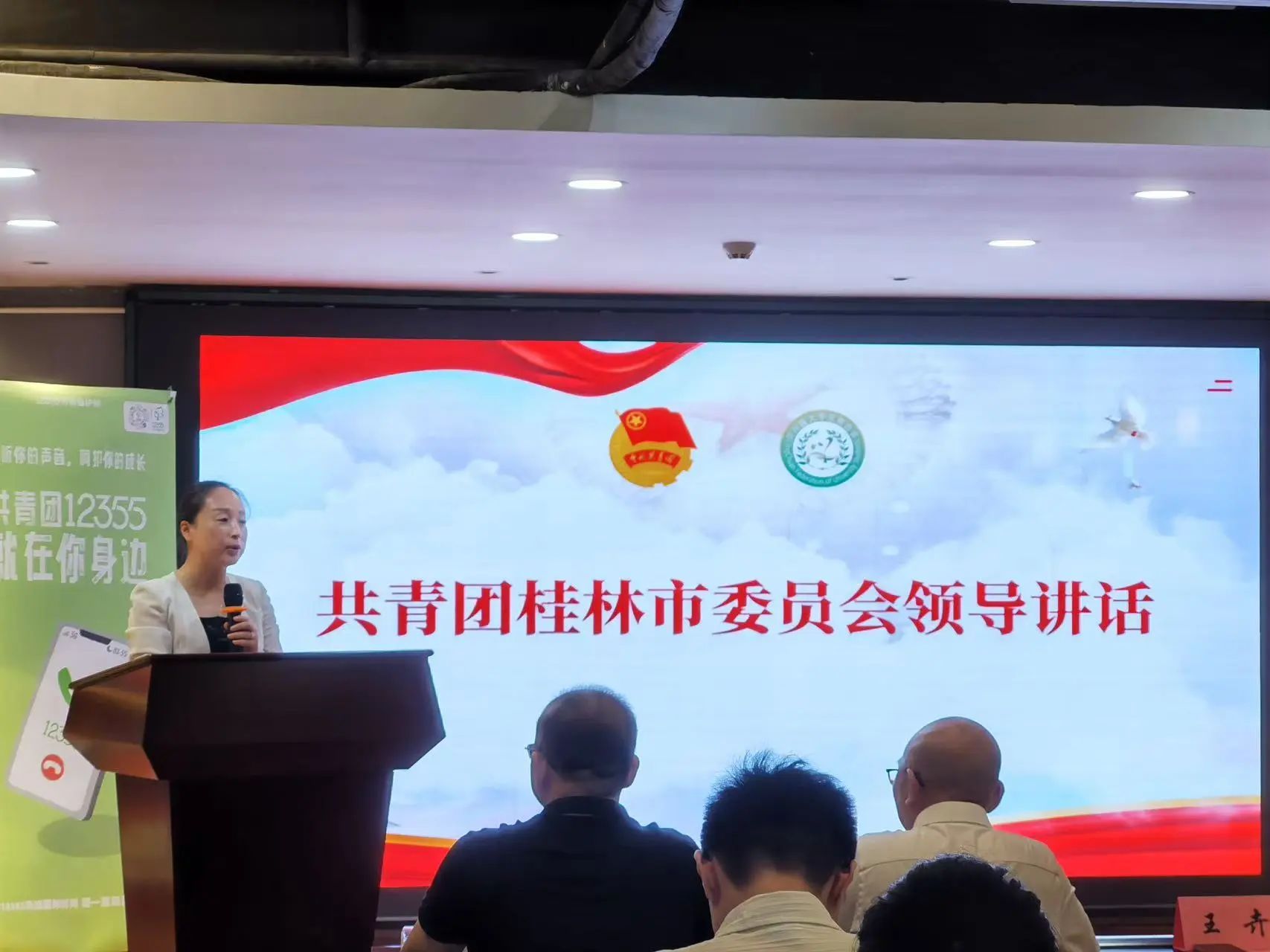 A leader representative gives a speech at a podium in front of a large presentation screen A leader representative gives a speech at a podium in front of a large presentation screen